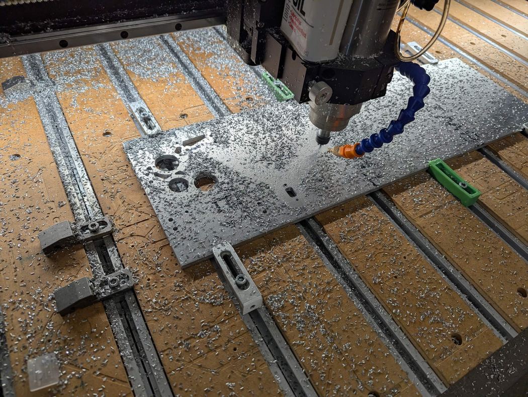 A 6061 aluminium plate being cut on the CNC router, chips across the bed and coolant running at the tool